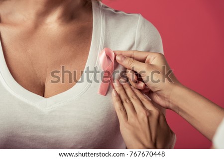 Women against breast cancer. Cropped image of girl putting a pink ribbon on woman's chest, on red background