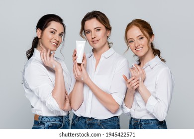 Women Applying Hand Cream And Smiling At Camera Isolated On Grey