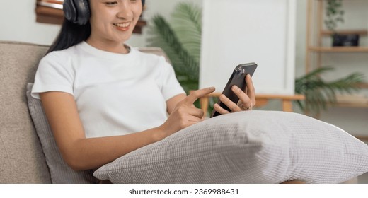 Women asian sitting on sofa and wearing headphone to listen music on smartphone in lifestyle at home - Shutterstock ID 2369988431