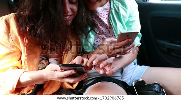 \
Women in backseat of car\
looking cellphone device, girlfriend spontaneous hiding screen from\
friend