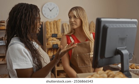 Women bakers discuss orders in a cozy bakery, surrounded by fresh bread and pastries, wearing aprons and standing by a computer in an indoor cafe setting. - Powered by Shutterstock