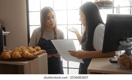 Women bakers discussing work in an indoor bakery setting, surrounded by fresh pastries, emphasizing teamwork and collaboration in a shop environment. - Powered by Shutterstock