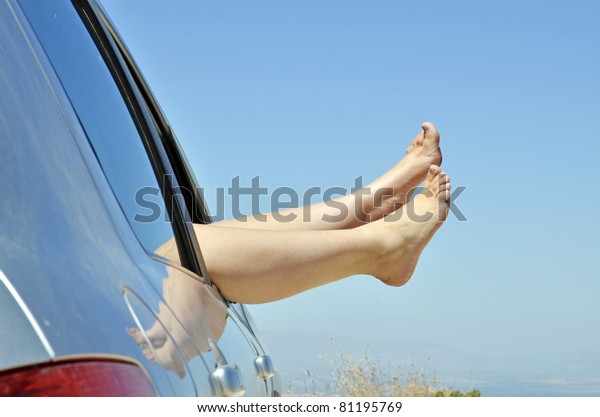 women with bare feet out the window of the car
road on vacation. Concept of happiness and relaxation during the
trip in the summer