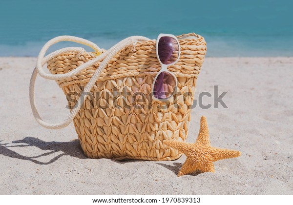 Women\
is beach accessories on the sand for a summer vacation concept.\
Straw bag, sunglasses, starfish. Travel\
background.