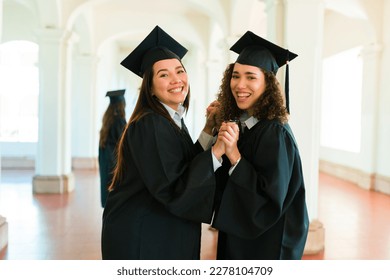 Women best friends with graduation gowns looking cheerful holding hands and celebrating getting university diplomas - Shutterstock ID 2278104709