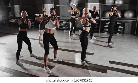 Women in black and white sportswear on a real group body Combat workout in the gym train to fight, kickboxing with a trainer