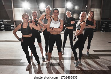 Women In Black And White Sportswear On Group Workout In Gym With Trainer. Powerful Fitness Girls With Sports Bodies Posing Like Bodybuilders