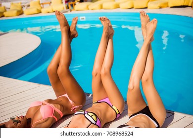 Women body care, pedicure, epilation, beauty, health concept. Close up cropped shot of long female legs of three multi ethnic hot chics with perfect smooth soft skin, getting tanned at beach