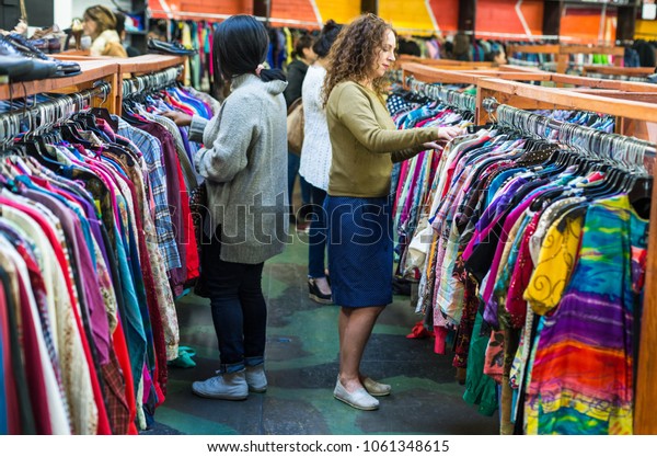 Women browsing through vintage clothing in a\
Thrift Store.
