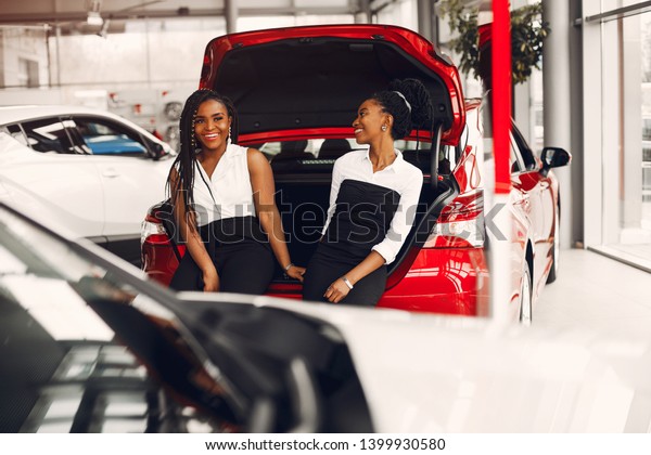 Women buying the car. Ladies in a car salon. Black\
girls near red car