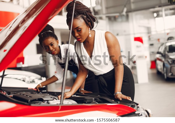 Women buying the car. Ladies in a car salon. Black\
girls near red car