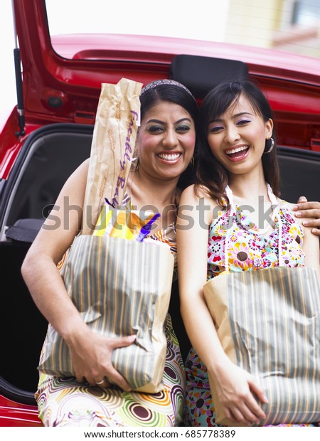 Women carrying grocery bags at supermarket car\
park, smiling and\
laughing