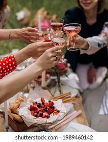 women clink glasses with rose wine at an outdoor party. female hands hold transparent glasses with pink champagne at a picnic. - Shutterstock ID 1989460142