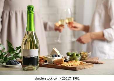 Women clinking glasses indoors, focus on table with bottle of wine and different snacks. Space for text