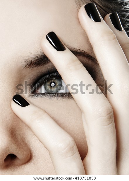 women\
close up smokey eyes make up and black nail\
polish