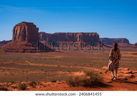 A women in colorful dress admiring the rock formations in Monument valley, USA. Blue sky and bright daylight. Orange rocks, spring time.
