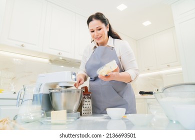 A Women Cook Adds A Butter To Prepare Dough Or Cream In A Mixer Bowl. Cooking Courses. Bread And Dessert Recipes. Family Business. Online Lessons For Cooks.