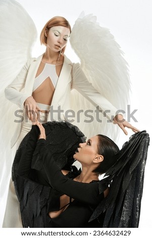 women in costumes of angel and demon looking at each other on white, redemption concept