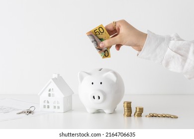 Women counting Australian Dollar coins next to a piggy bank and model house 