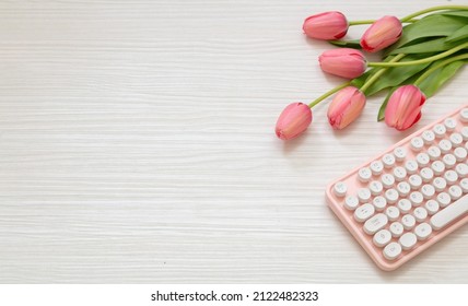 Women day. Pink tulip and computer laptop keyboard on white wood, top view, copy space.