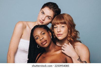 Women with different skin tomes looking at the camera in a studio. Group of confident young women feeling comfortable in their natural skin. Three body positive young women standing together.