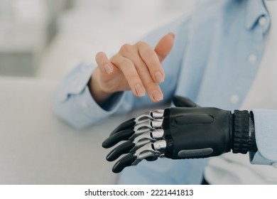 Women with disability movements using bionic prosthesis of hand, touching, customizing artificial limb. Close up of womans healthy and prosthetic hands. Disability, high tech medical care concept. - Shutterstock ID 2221441813