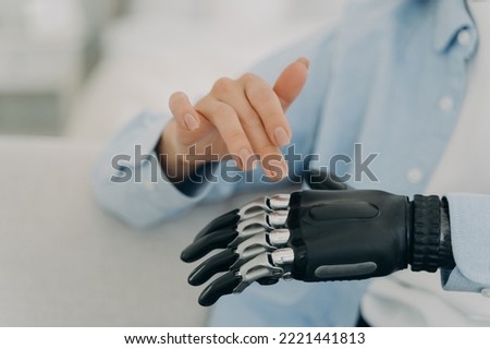 Women with disability movements using bionic prosthesis of hand, touching, customizing artificial limb. Close up of womans healthy and prosthetic hands. Disability, high tech medical care concept.