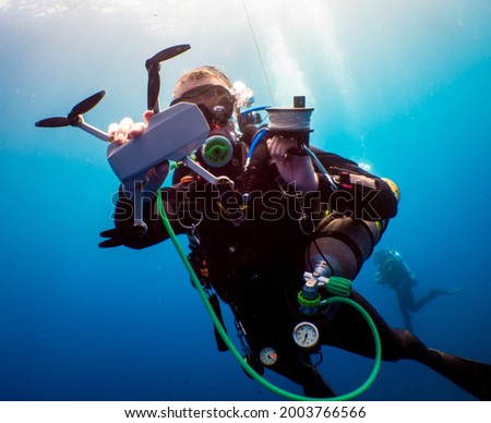 Women diver with drone underwater shooting on a blue background whith bubbles. Diver with tech equipement