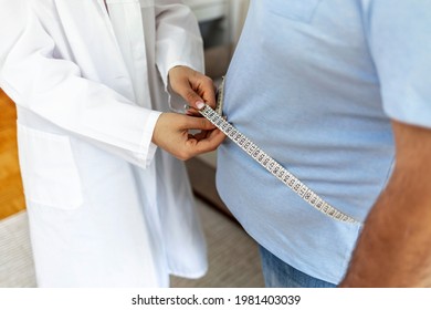 Women doctor measuring overweight man in clinic. Young female doctor measuring fat layer of overweight man with tailor tape in clinic. Eating, diet and unhealthy life concept. Copy space.  
