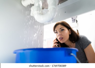 Women Doing Emergency Plumber Phone Call In Kitchen At Home