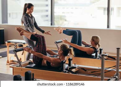 Women doing pilates exercises lying on pilates workout machines while their trainer guides them. Two fitness women being trained by a pilates instructor. - Powered by Shutterstock