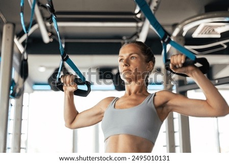 Women doing pull ups training arms with trx fitness straps in the gym. Upper body training. Back view
