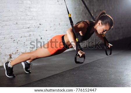Women doing push ups training arms with trx fitness straps in gym
