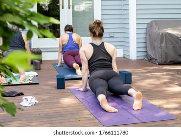 Women Doing A Virtual Yoga Class At Home Outside During COVID-19 Coronavirus Pandemic.  Social Distancing While Practicing Yoga.