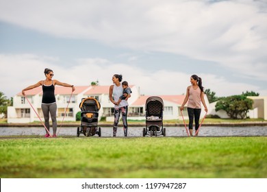 Women doing workout in park bringing their kids in strollers. Young mothers doing stretching exercise using stretch banks in park beside a lake. - Powered by Shutterstock