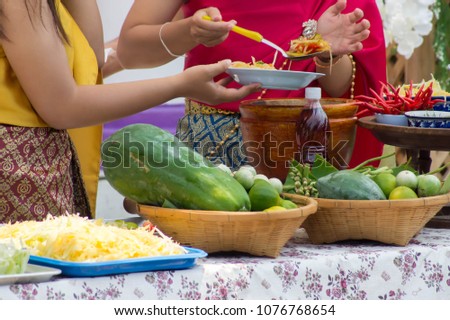 Women dress up retro, are cooking Thai salad and have a lot of ingredients on the tray.