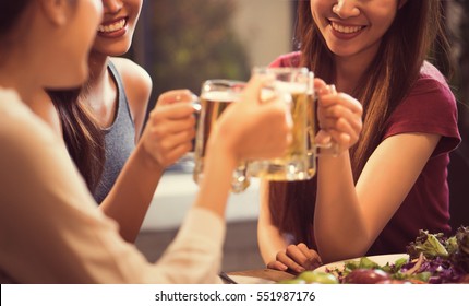 Women are drinking beer and the clink glasses in a restaurant.