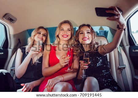 Women drinking champagne and make selfie in a limousine car.