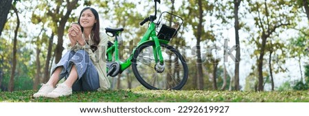 Women drinking coffee and watching view while sitting on grass to resting after cycling in park.