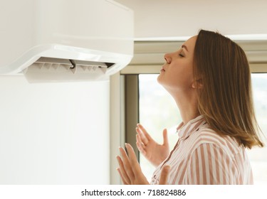 Women dying from the heat standing in front of the air conditioner. - Shutterstock ID 718824886