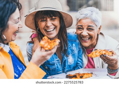 Women eating pizza outdoors at city - Happy three senior having fun together outside on street and laughing with food- Friendship and lifestyle concept - Powered by Shutterstock