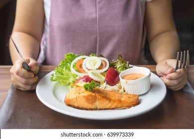 Women Eating Salmon Steak On White Plate On Table Hand Holding Knife And Fork