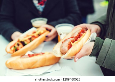 Women Eating Sausage At Street Food Festival. Czech Market In Prague. Street Food At Winter Time In European Town. Travelling And Lifestyle Concept. Festival Of Street Food. Traveler Snacks Sausage