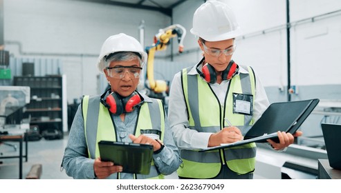 Women, engineers and tablet with team for checklist, inspection and paperwork at factory. Female employees, collaboration and production with quality control, manager and robotics at warehouse