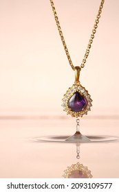 Women fashion, beautiful 24K gold necklace with water drop pendant and natural purple amethyst stone surrounded with small diamonds hanging on the water with pink background
