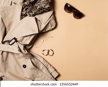 Women Fashion Clothes And Accessories Flat Lay, Beige Trench Coat With Bag, Glasses, Denim And Western Boots On Beige Background, Top View, Copy Space