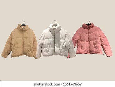 Women fashion down jacket pattern. A selection of different jackets on hangers isolated on beige background. Winter clothes pattern. Composition of clothes. Flat lay. Padded coat