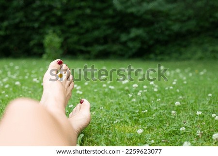 Women Feet with red nail polish laying in garden grass with a lot of daisy flowers an relax