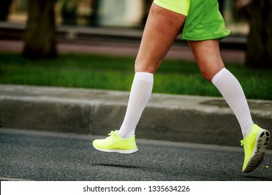 Women Feet In White Compression Socks And Bright Green Running Shoes