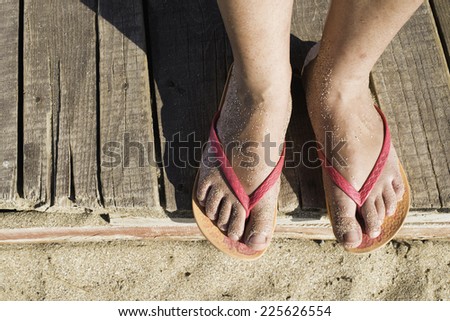 Women foots on the beach. Pink thongs. Wooden board